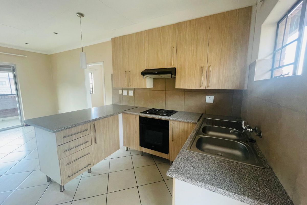 A clean, functional kitchen featuring light wood-finish cabinetry, granite-look countertops, a built-in oven and hob, and a convenient breakfast bar area.