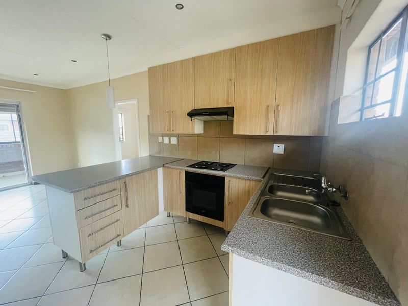 A clean, functional kitchen featuring light wood-finish cabinetry, granite-look countertops, a built-in oven and hob, and a convenient breakfast bar area.