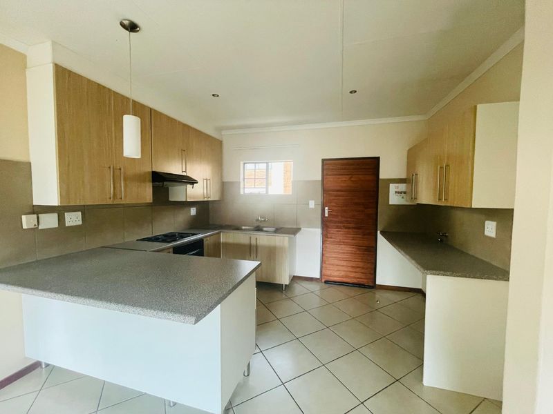 A clean, functional kitchen featuring laminate cabinetry, stone-look countertops, built-in oven, hob, extractor fan, and tiled flooring.