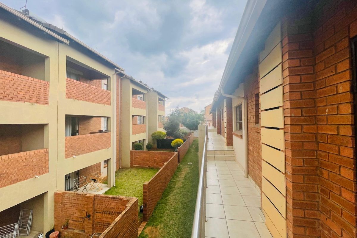 View from an upper-level tiled balcony overlooking the communal garden area and adjacent townhouse blocks with brick facade detailing.