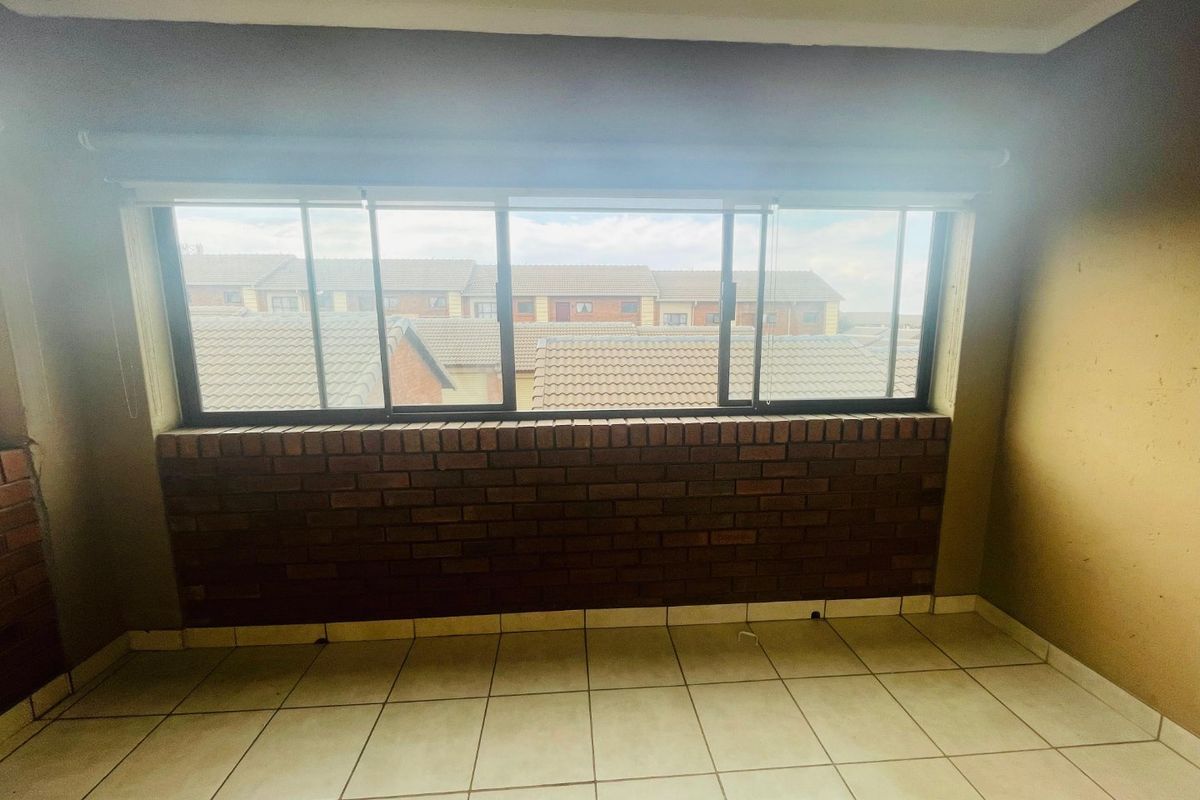 An empty bedroom featuring tiled flooring, a brick feature wall, and a large sliding window with views of the surrounding townhouse complex.