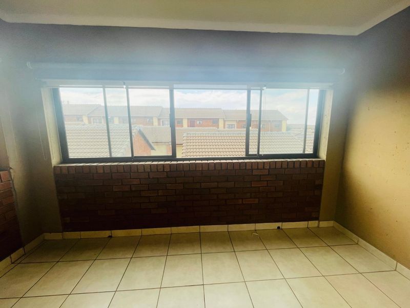 An empty bedroom featuring tiled flooring, a brick feature wall, and a large sliding window with views of the surrounding townhouse complex.