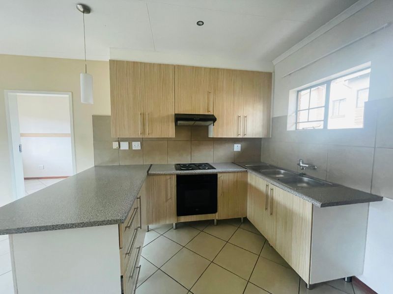 Functional kitchen featuring light wood-look cabinetry, granite-style countertops, built-in oven, hob, extractor fan, and a double stainless steel sink with tiled splashbacks.