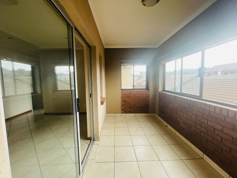 A covered patio area featuring tiled flooring, exposed brick accents, and large sliding glass doors leading into the main living space.