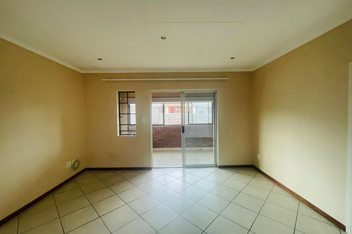 An empty, neutrally painted living room featuring tiled flooring, recessed lighting, and a sliding glass door providing access to an outdoor balcony area.