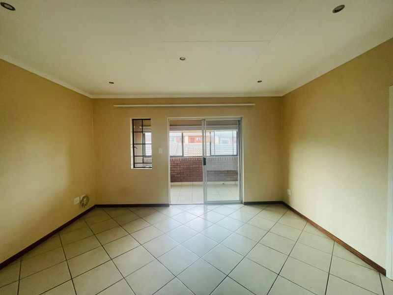 An empty, neutrally painted living room featuring tiled flooring, recessed lighting, and a sliding glass door providing access to an outdoor balcony area.