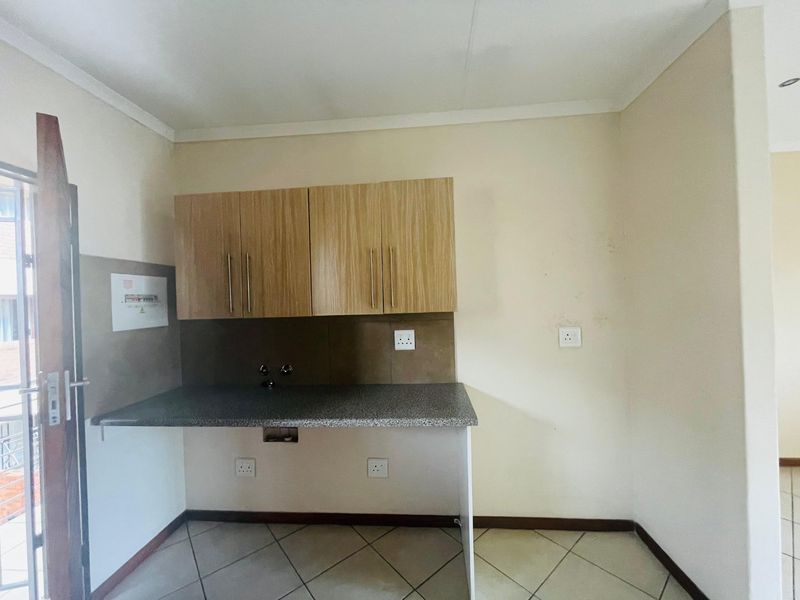 A compact kitchen area featuring laminate cabinetry, a stone-look countertop, tiled splashback, and ceramic floor tiles, presenting a functional space ready for updates.