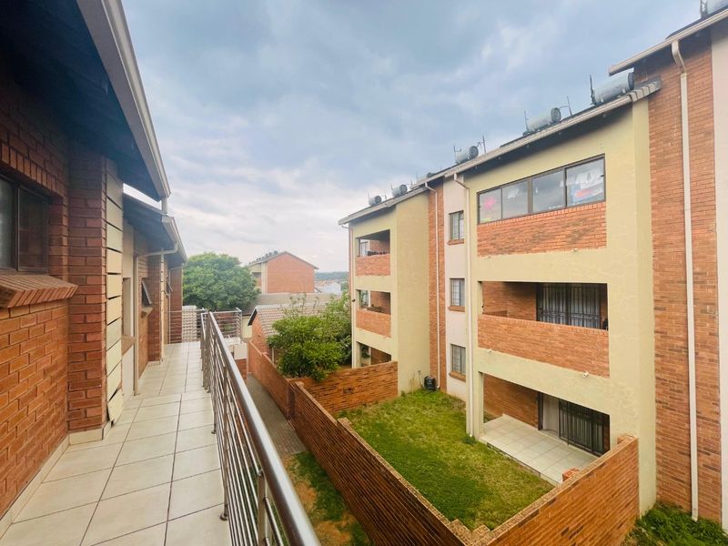 An elevated balcony with tiled flooring and stainless steel balustrades, overlooking a communal garden area and adjacent townhouse units.