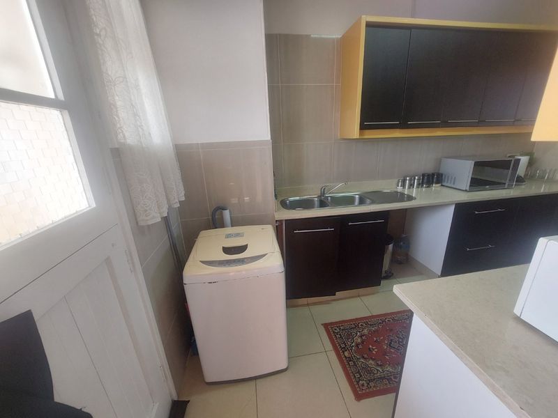 A functional kitchen area featuring dark cabinetry, a double bowl stainless steel sink, tiled backsplash, and tiled flooring.