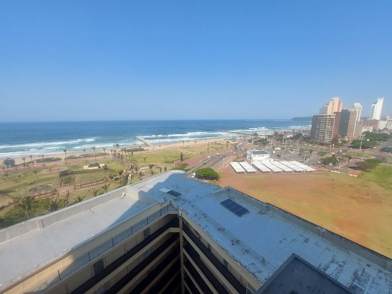 Elevated coastal view overlooking the beach, promenade, and surrounding urban landscape from a high-rise apartment perspective.