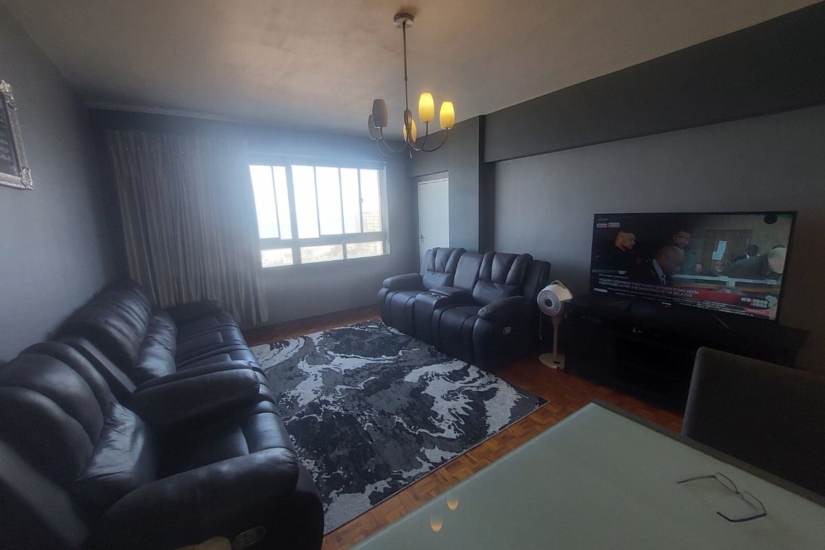 A comfortable living room featuring parquet flooring, a large window allowing natural light, and a central ceiling light fixture.