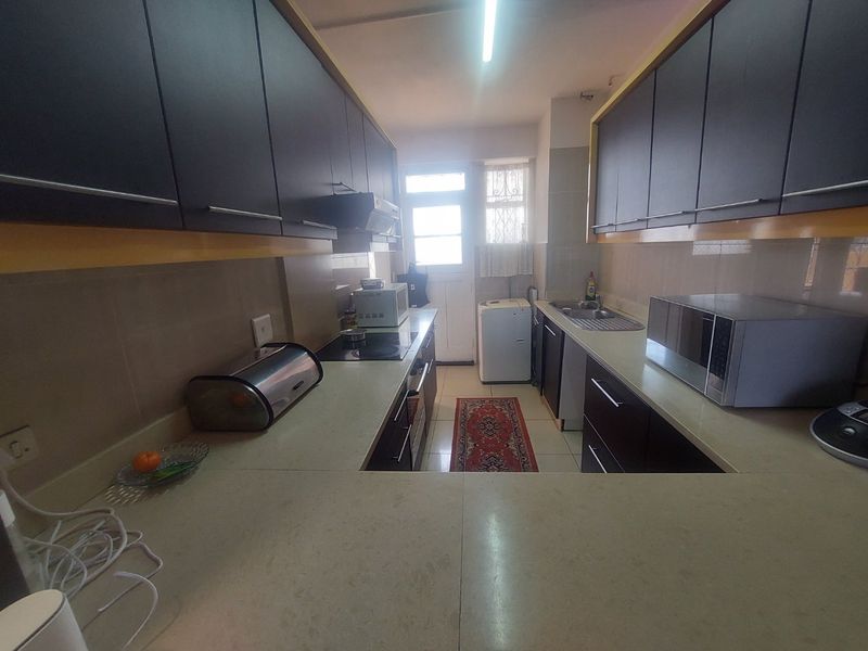 A functional galley-style kitchen featuring dark cabinetry, stone countertops, integrated cooktop, and a stainless steel sink with direct access to an exterior door.
