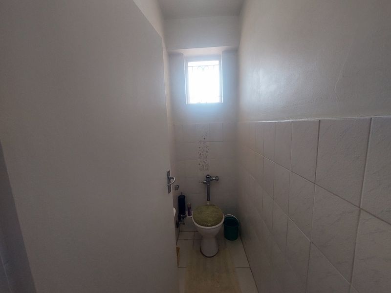 A compact guest bathroom featuring ceramic wall and floor tiling, a standard flush toilet, and a small window with security bars.