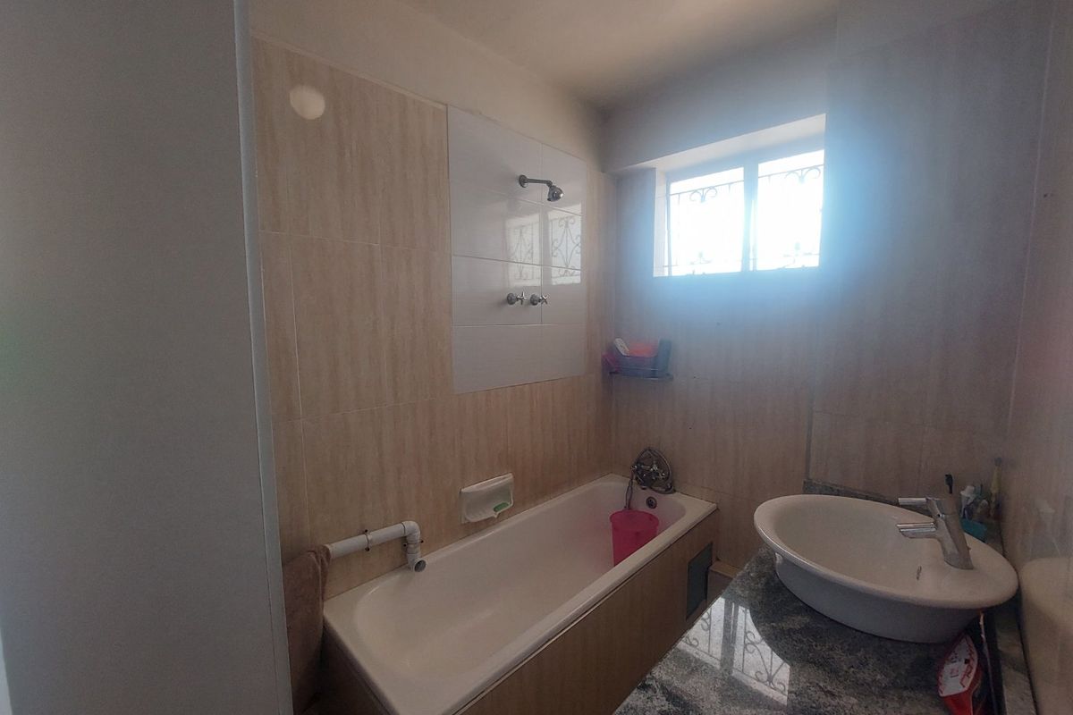 A functional bathroom featuring a bathtub with shower head, a vanity basin with granite countertop, and tiled wall finishes.