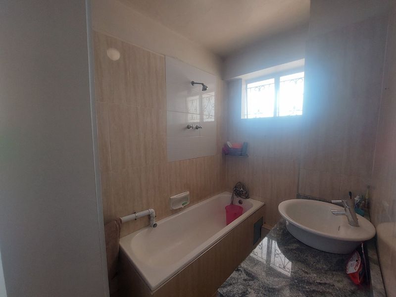 A functional bathroom featuring a bathtub with shower head, a vanity basin with granite countertop, and tiled wall finishes.