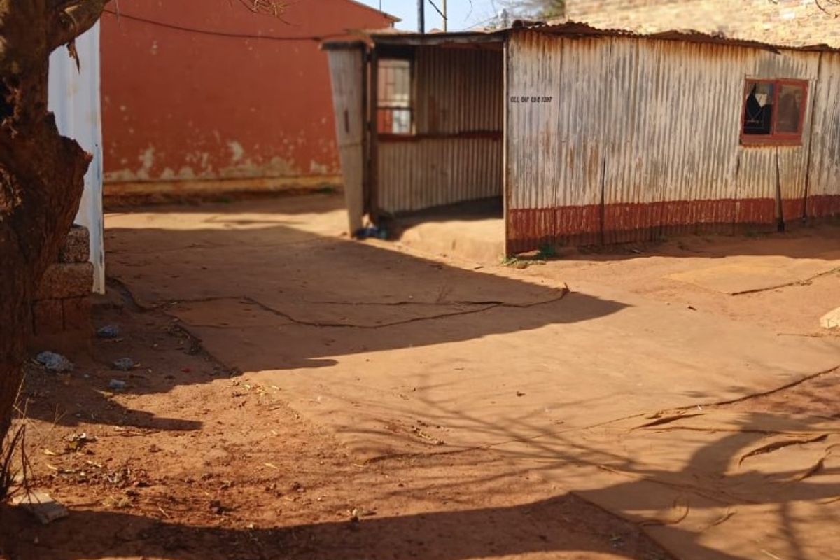 An exterior view of a rear yard featuring a corrugated iron structure and an unpaved ground surface.