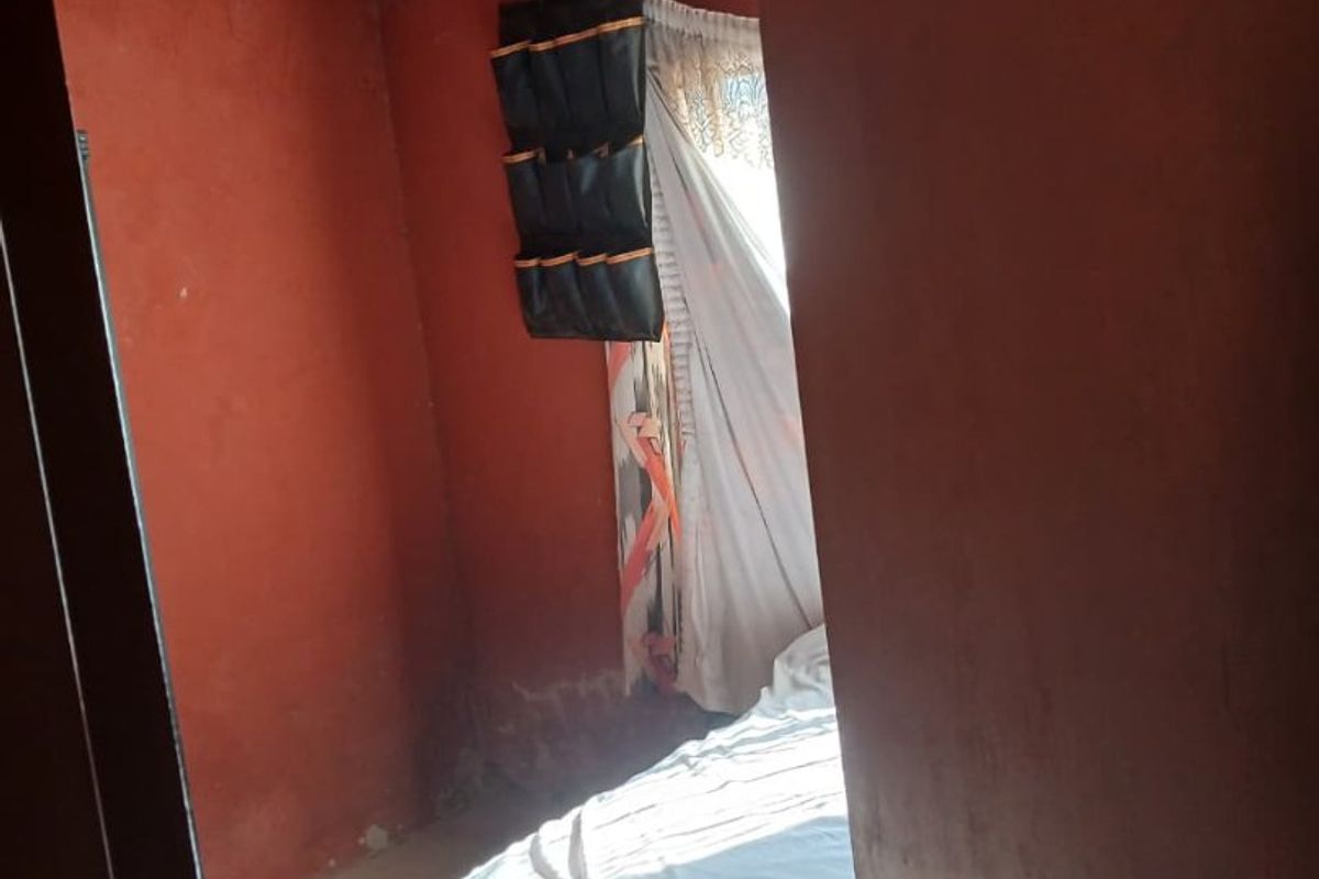 A bedroom featuring a corrugated metal ceiling and painted walls showing signs of wear and surface deterioration.