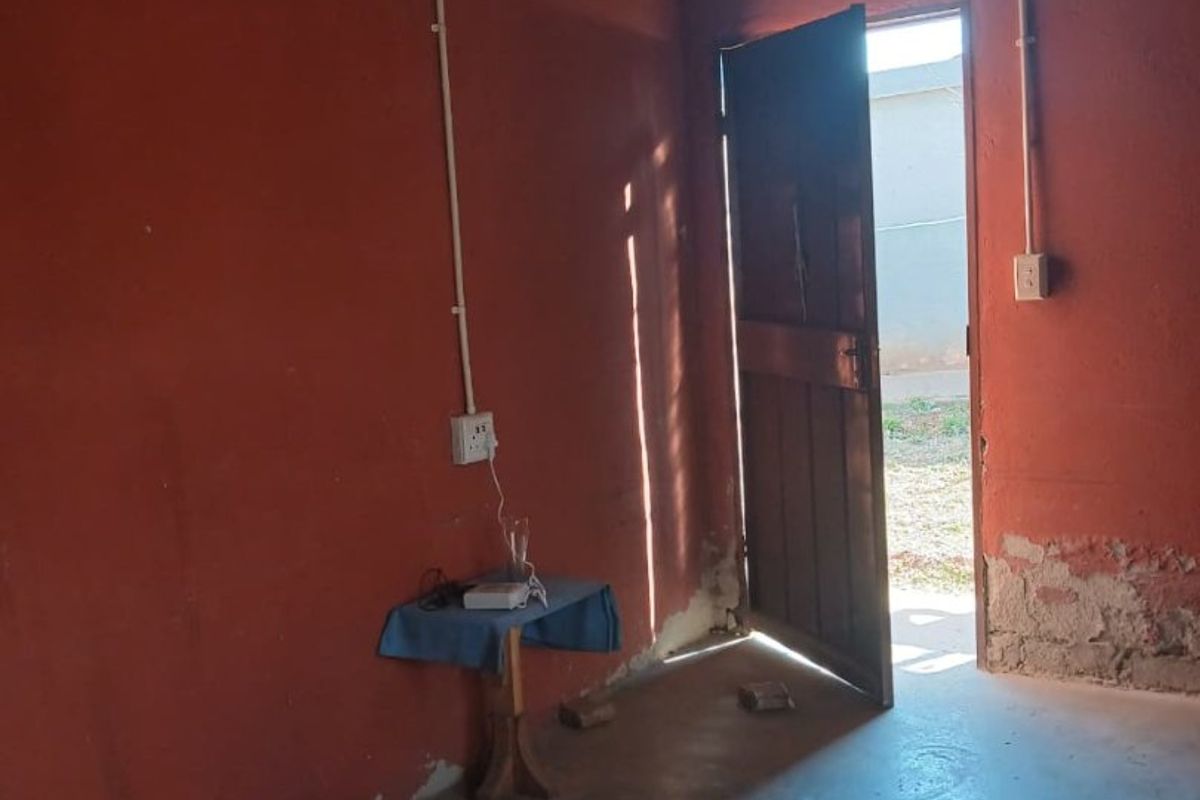 A basic bedroom space featuring exposed electrical conduit, a corrugated metal ceiling, and direct access to the exterior through a timber door.