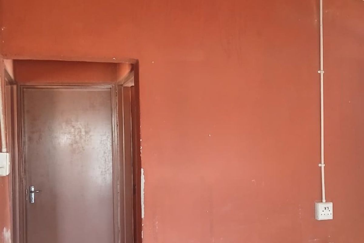 An interior space featuring exposed corrugated metal roofing, surface-mounted electrical conduits, and a simple internal door with visible wear on the wall finishes.