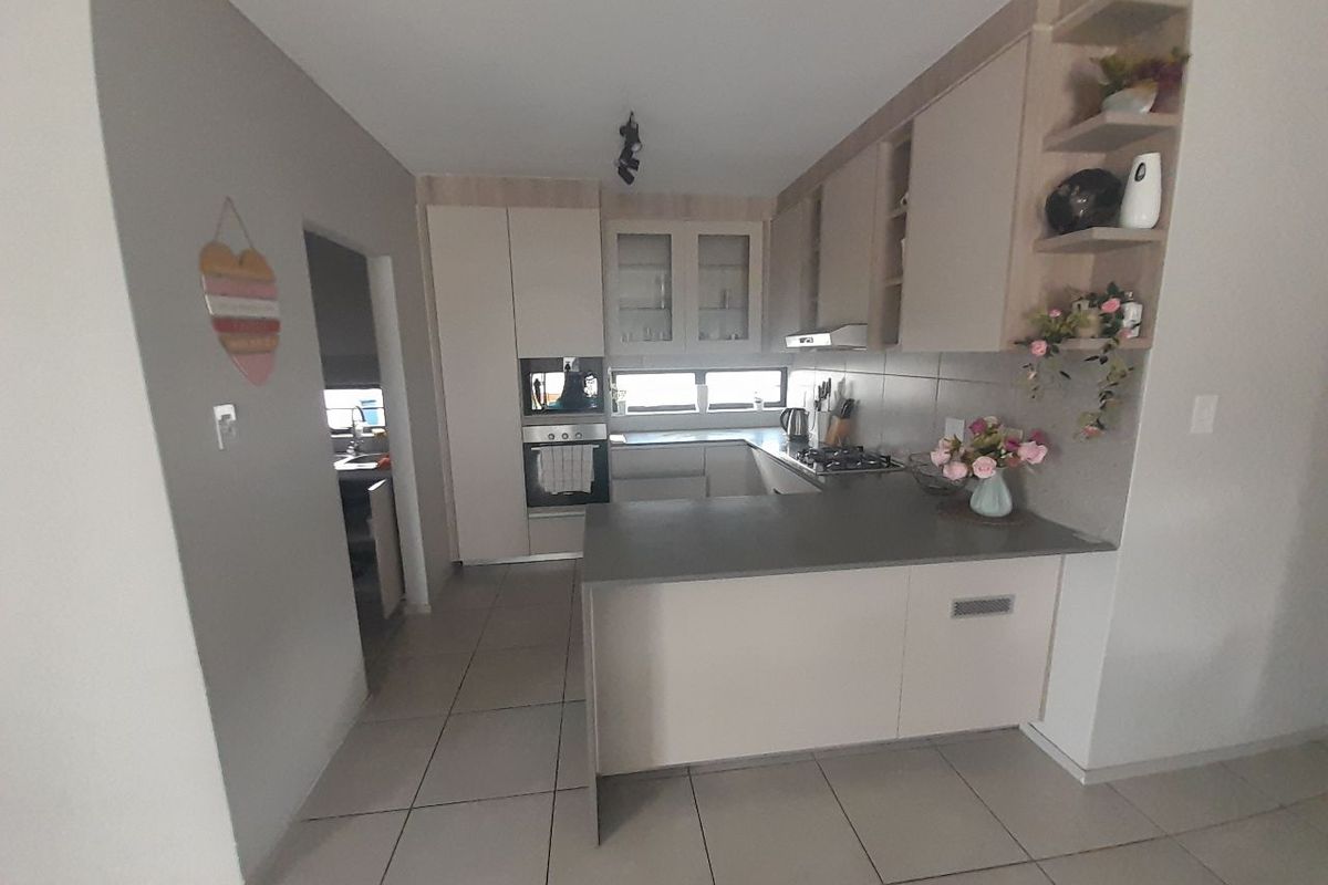 Modern kitchen featuring neutral cabinetry, stone countertops, built-in oven, gas hob, and tiled flooring, with an adjacent scullery area.