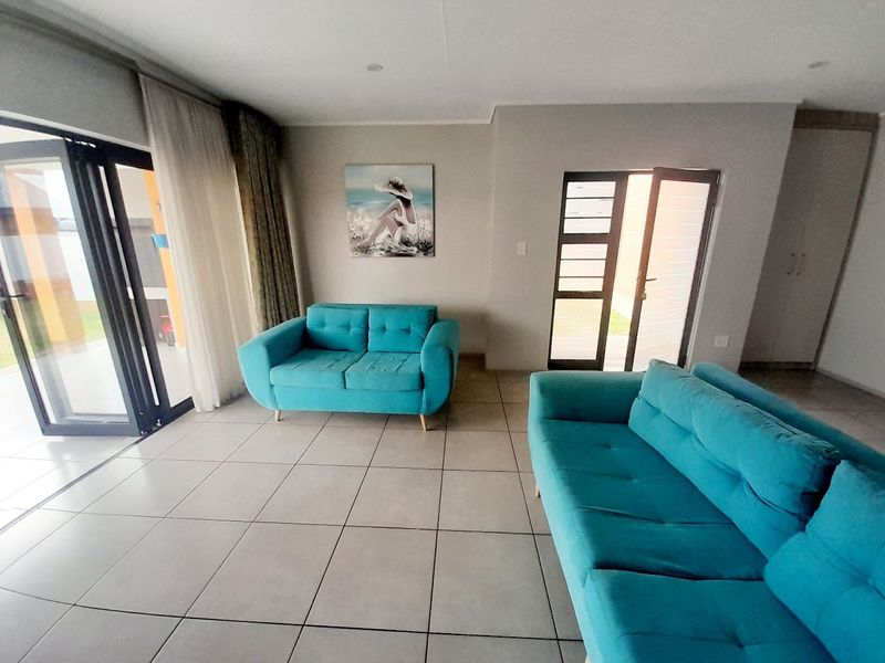 A bright living room featuring large format floor tiles, a sliding glass door leading to the patio, and a secure entrance door.