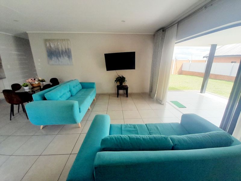 Bright living room featuring large format floor tiles and a wide sliding glass door providing seamless access to the outdoor patio and garden area.