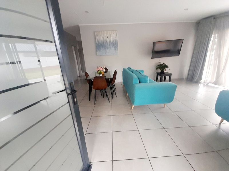 An open-plan living and dining area featuring neutral tiled flooring, recessed lighting, and access to an outdoor space via a sliding glass door.