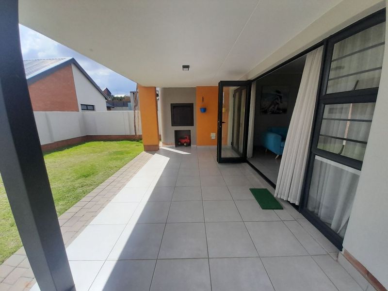 A covered patio featuring tiled flooring and a built-in braai, providing seamless access to the garden through large sliding doors.