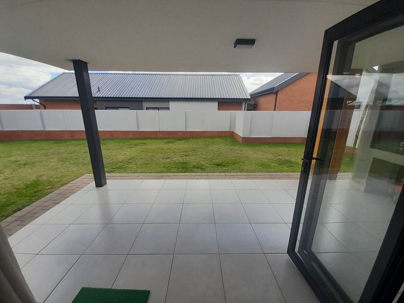 A modern covered patio featuring large format floor tiles, a support pillar, and bi-fold doors leading to a private garden with a boundary wall.