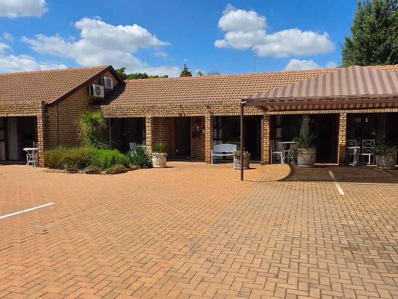 Front view of a commercial property featuring a brick facade, tiled roof, and a paved parking area with a covered entrance section.