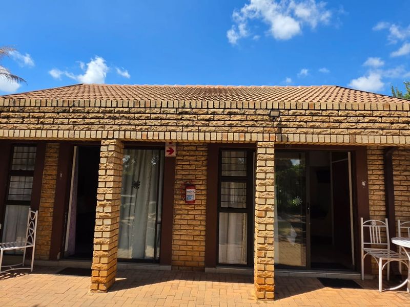 A well-maintained commercial exterior featuring a face brick facade, tiled roof, and paved patio area with dual sliding glass door entrances.