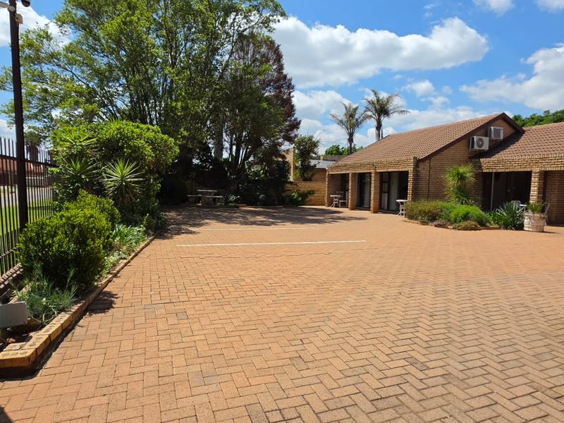 A well-maintained commercial property exterior featuring extensive brick paving, secure metal fencing, and a brick facade with multiple access points and air conditioning units.