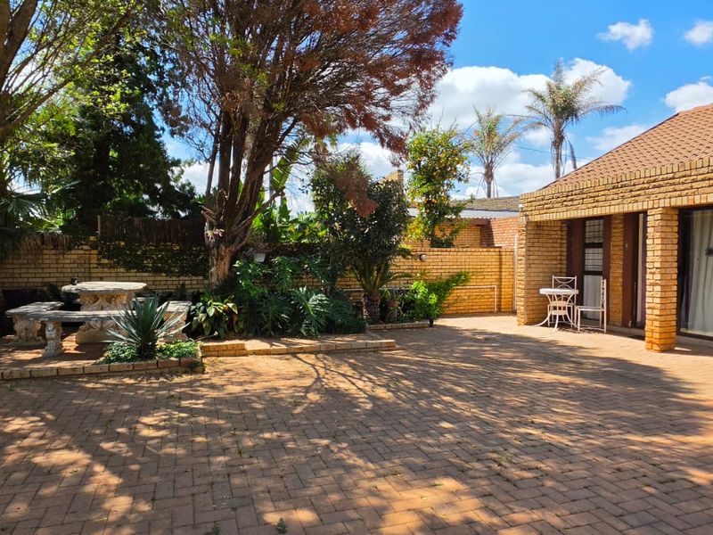 A spacious rear courtyard featuring brick paving, a covered patio area, and established garden landscaping with a facebrick building exterior.