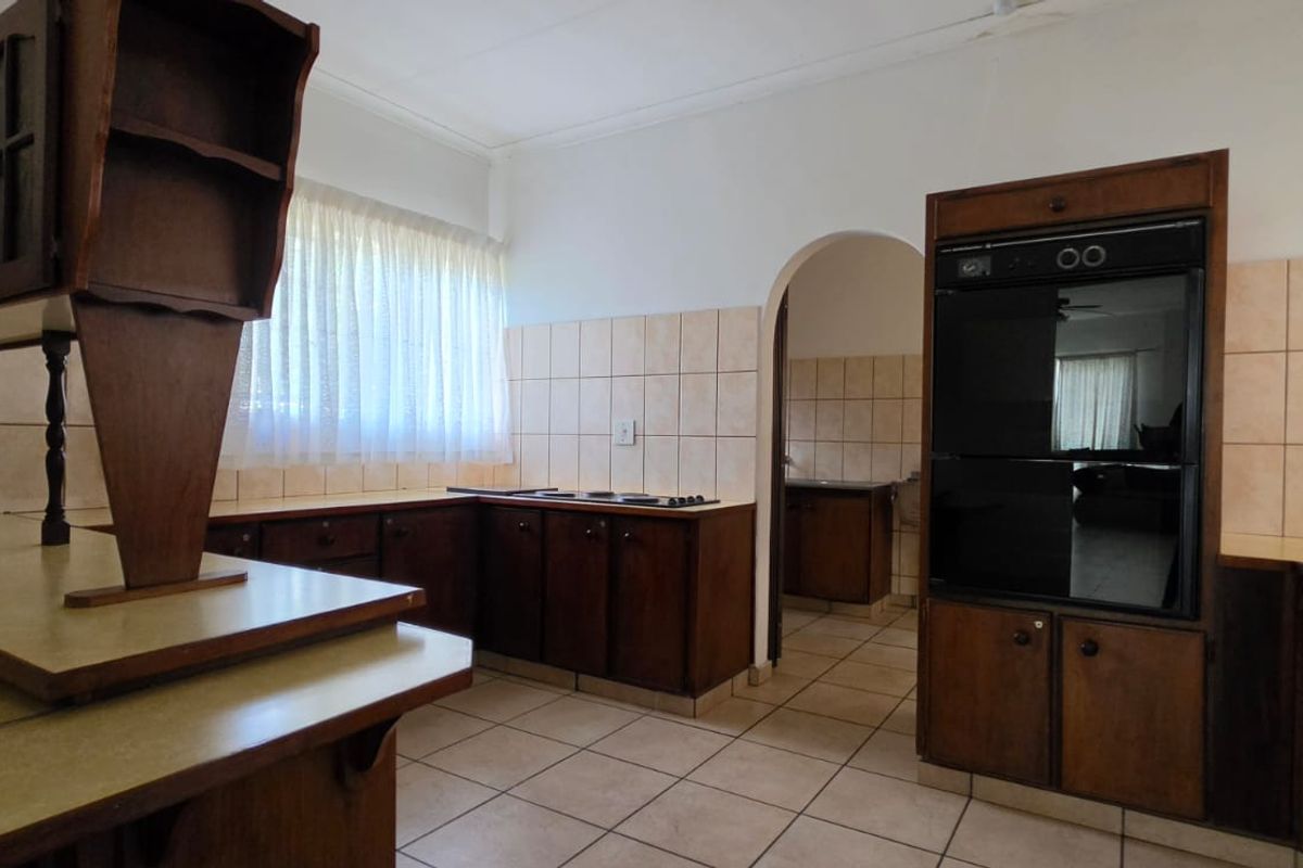 A functional kitchen featuring built-in wooden cabinetry, tiled backsplash, and a built-in oven, offering a classic layout with an adjoining archway.
