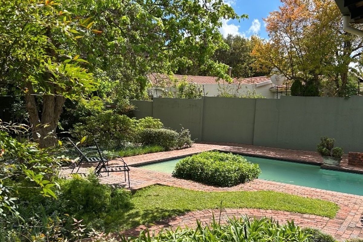 A private outdoor pool area featuring brick paving, established garden landscaping, and a solid boundary wall for privacy.
