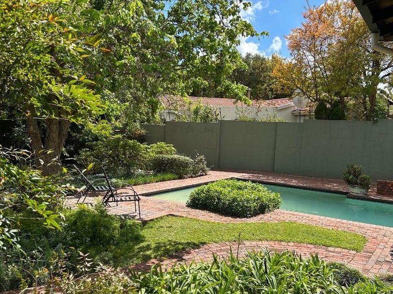 A private outdoor pool area featuring brick paving, established garden landscaping, and a solid boundary wall for privacy.
