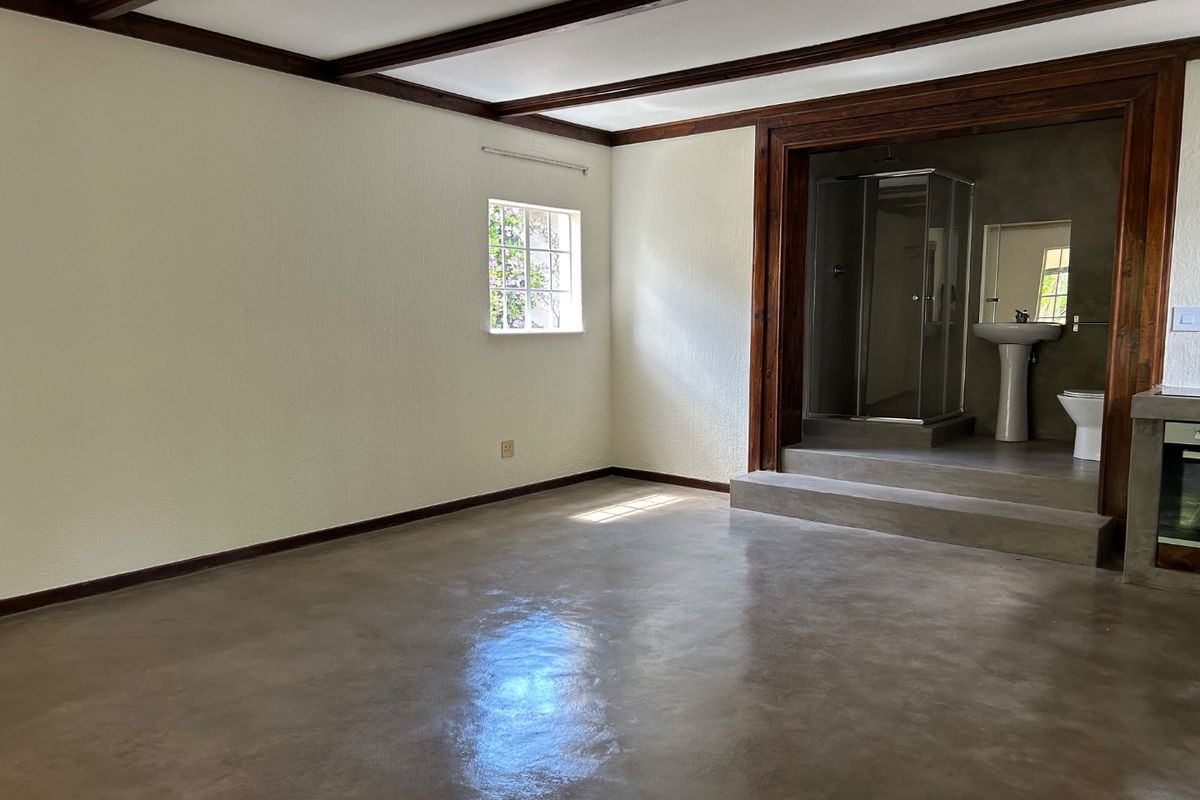 Open plan living area featuring polished concrete floors, exposed timber ceiling beams, and a raised platform leading to an integrated bathroom suite.
