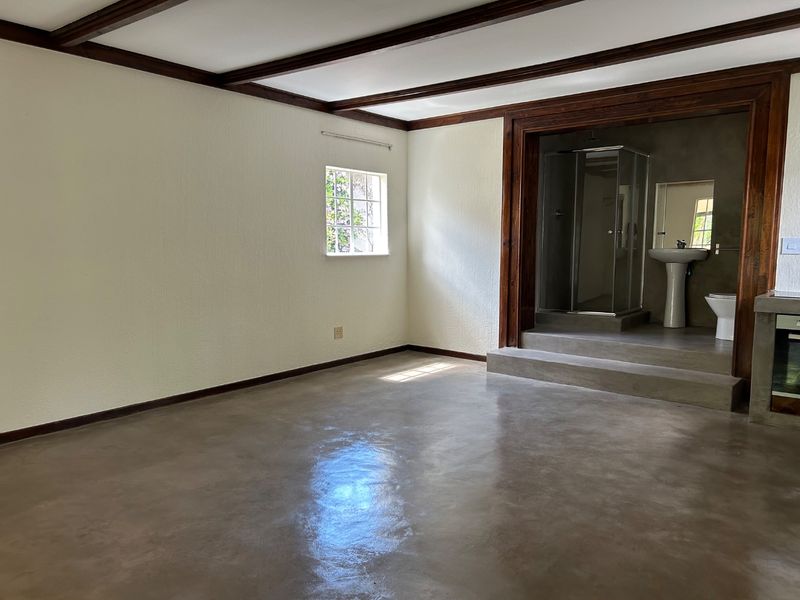 Open plan living area featuring polished concrete floors, exposed timber ceiling beams, and a raised platform leading to an integrated bathroom suite.