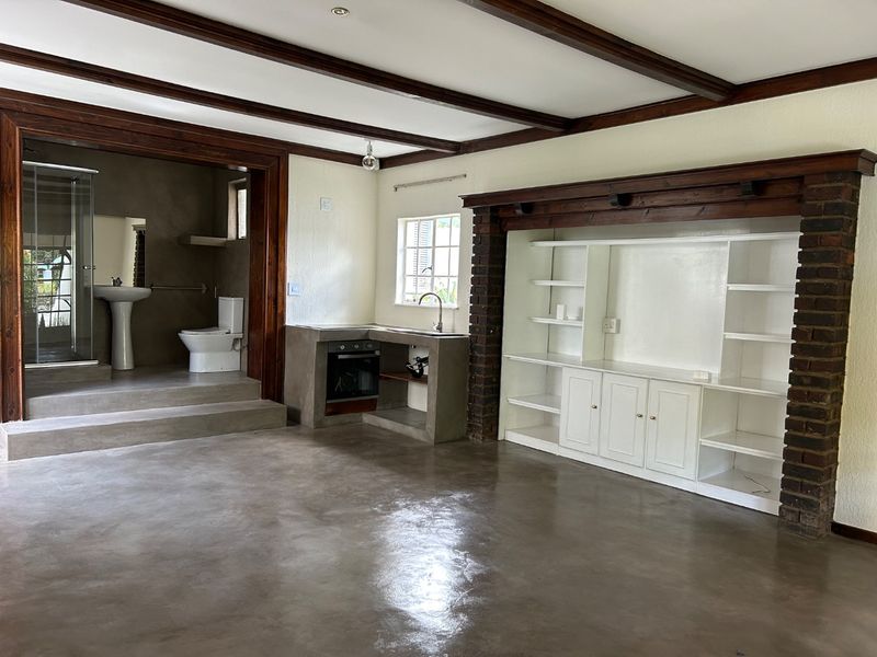 Spacious open-plan living area featuring polished concrete floors, exposed timber beams, a built-in brick fireplace, and an integrated kitchen and bathroom suite.