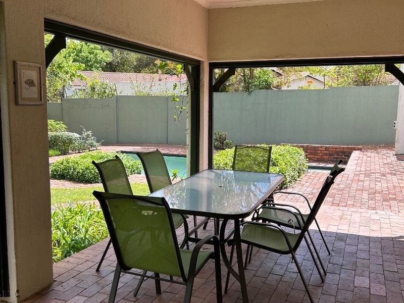 A covered outdoor patio featuring brick paving and direct access to the garden and pool area, ideal for alfresco dining.