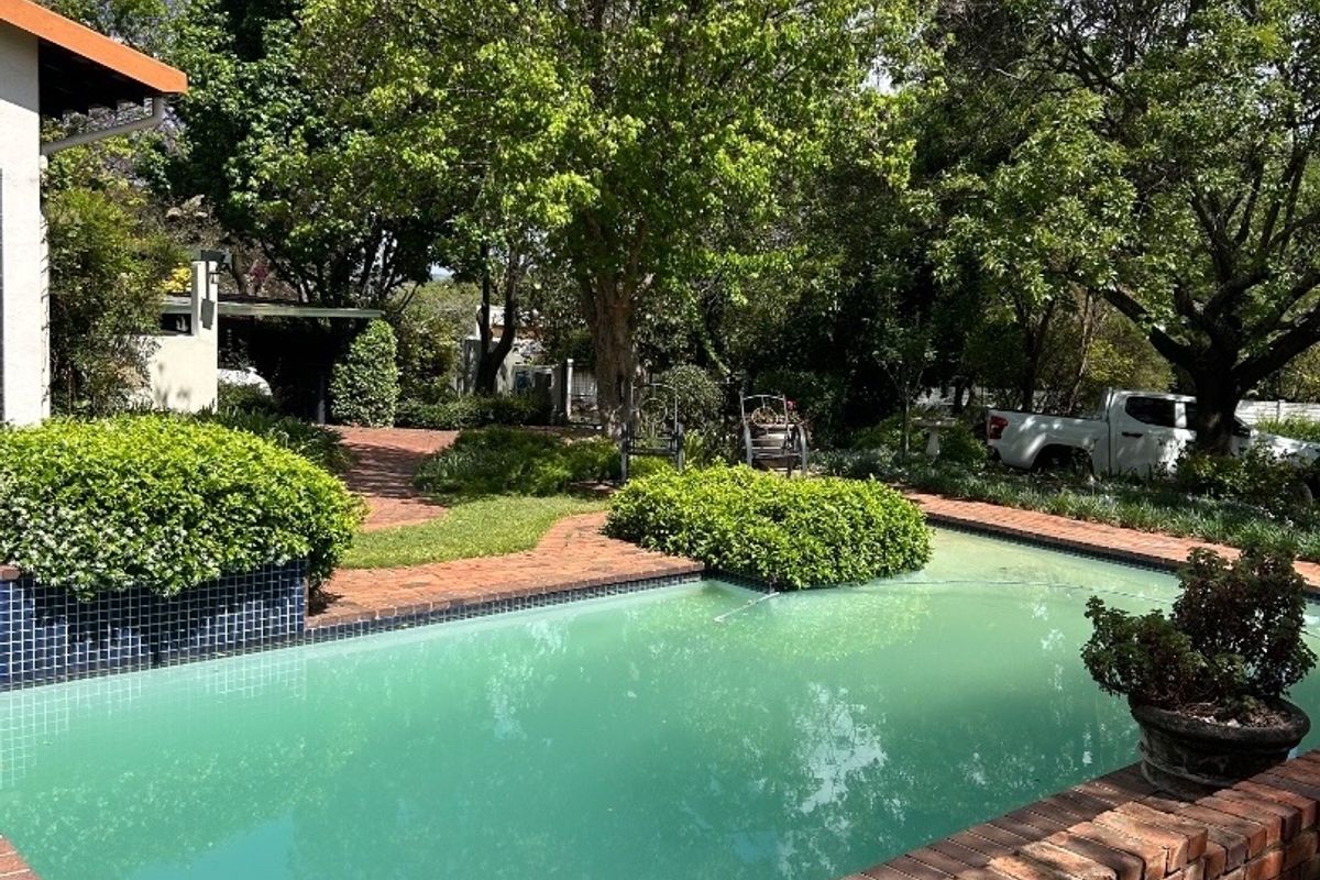Outdoor swimming pool area featuring brick paving and a brick retaining wall, set within a mature garden environment.