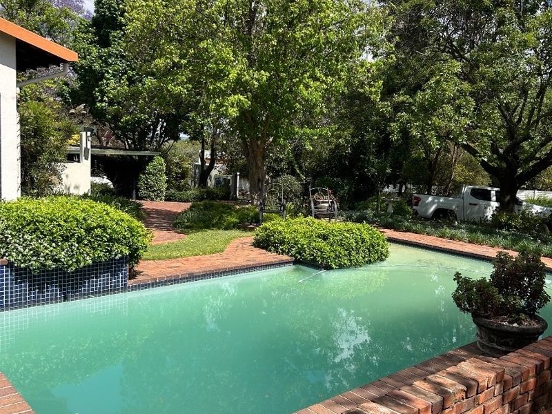 Outdoor swimming pool area featuring brick paving and a brick retaining wall, set within a mature garden environment.