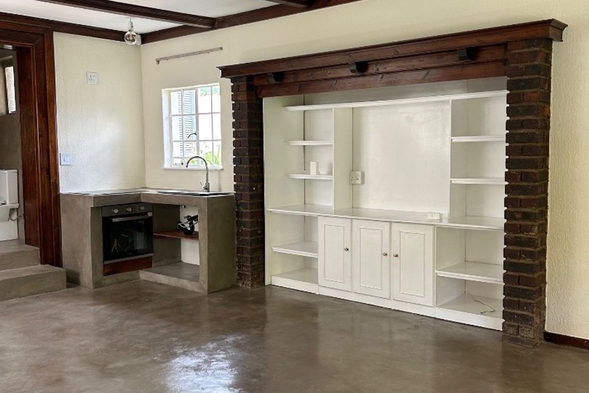 Spacious open-plan living area featuring polished concrete floors, exposed timber ceiling beams, and a unique built-in brick fireplace surround with integrated shelving.