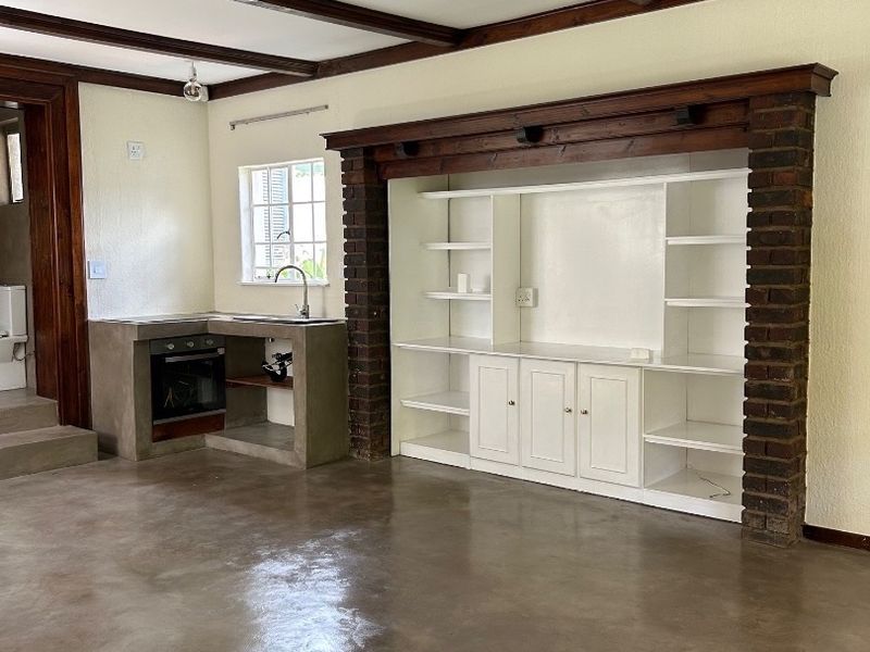 Spacious open-plan living area featuring polished concrete floors, exposed timber ceiling beams, and a unique built-in brick fireplace surround with integrated shelving.