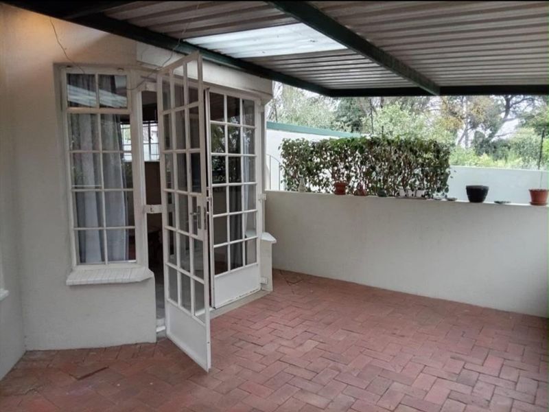 A covered patio area featuring brick paving, a metal roof structure, and white french doors leading into the apartment.