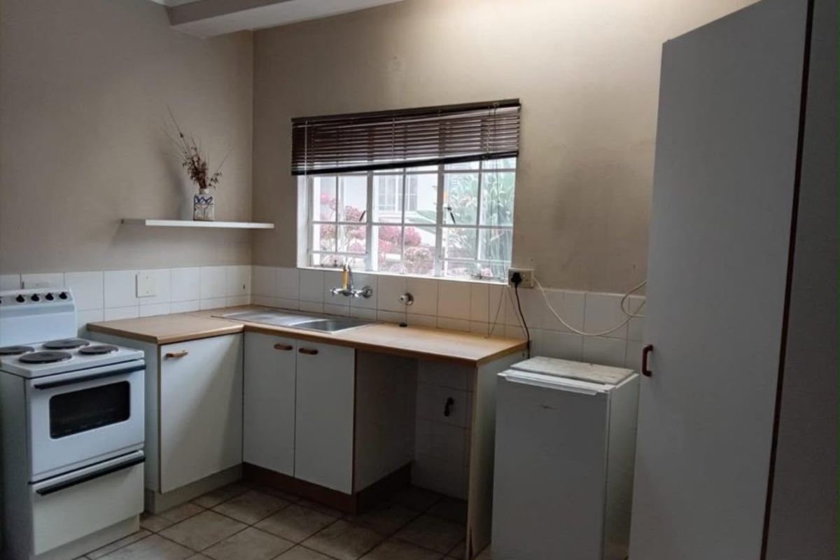 A functional kitchen featuring built-in cabinetry, laminate countertops, a stainless steel sink, and a freestanding stove with tiled flooring and backsplash.