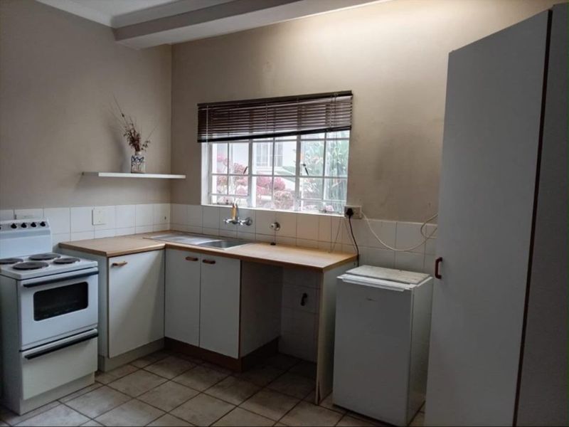 A functional kitchen featuring built-in cabinetry, laminate countertops, a stainless steel sink, and a freestanding stove with tiled flooring and backsplash.