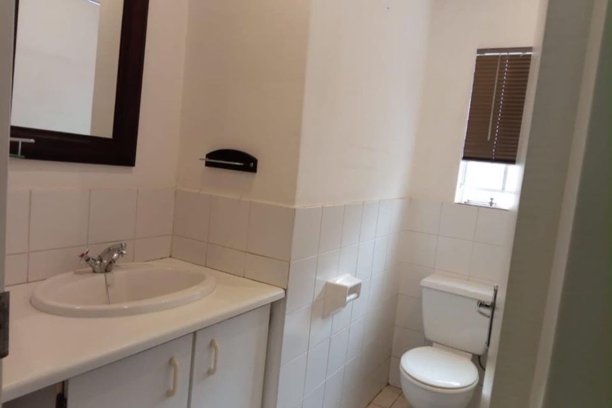 A functional bathroom featuring a vanity cabinet with a ceramic basin, wall-mounted mirror, and standard toilet, finished with white wall tiles.