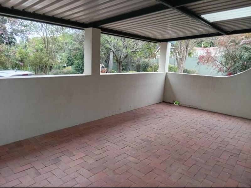 A covered outdoor patio area featuring brick paving and a corrugated metal roof, offering a functional space for outdoor relaxation.