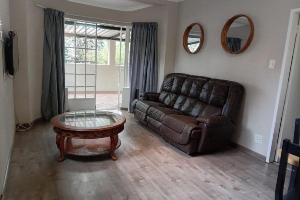 A comfortable living room featuring laminate flooring, coved ceilings, and a sliding glass door providing access to an outdoor patio area.